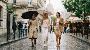 Three women walking down a damp Paris street wearing stylish rain-appropriate summer outfits.