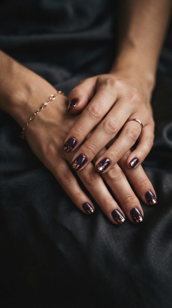 Deep plum glossy nails embellished with subtle rose gold foil flakes along tips.